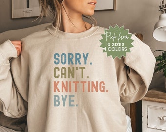 May include: A beige sweatshirt with the text "SORRY. CAN'T. KNITTING. BYE." in colorful letters. The sweatshirt is available in 6 sizes and 4 colors.