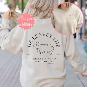 May include: A beige sweatshirt with a black graphic design on the back. The graphic features a sheep with the text "He Leaves the Ninety-Nine to Find the One".