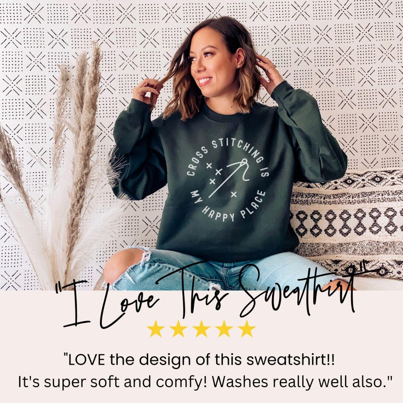 May include: Dark green sweatshirt with the text "Cross Stitching is My Happy Place" in a white circular design. The sweatshirt is long-sleeved and worn by a person. The image includes text that says "I Love This Sweatshirt".