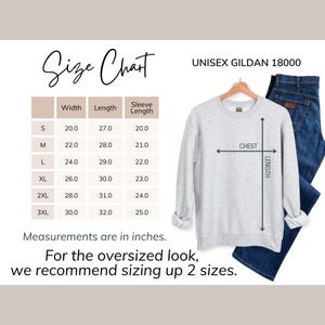 May include: A light gray Gildan 18000 unisex sweatshirt with a size chart. The chart shows measurements in inches for width, length, and sleeve length, ranging from size small to 3XL. The text recommends sizing up for an oversized fit.