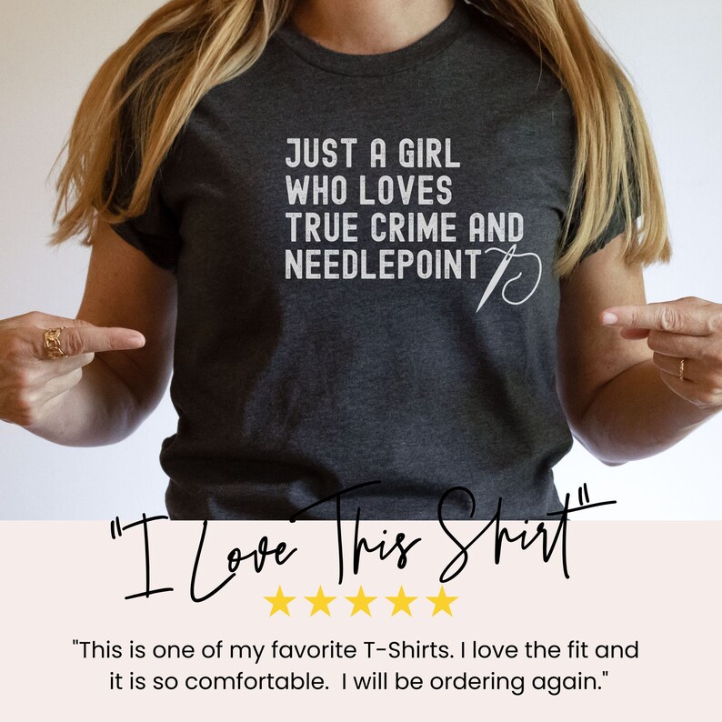 May include: A dark gray t-shirt with the text "Just a girl who loves true crime and needlepoint" in white. A white needle and thread design is next to the text. The text "I Love This Shirt" is written in black cursive with five gold stars below it.