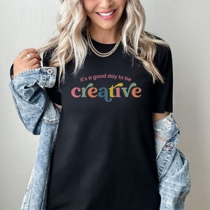 May include: Black t-shirt with the text "It's a good day to be creative" in colorful letters.