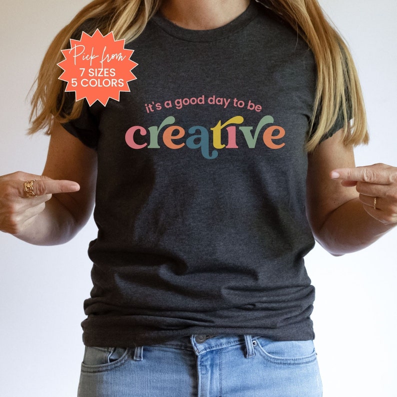 May include: A dark grey t-shirt with the text "it's a good day to be creative" in colorful letters. The text is in a retro font style.