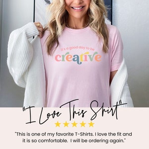 May include: A pink t-shirt with the text "it's a good day to be creative" in colorful letters. The shirt is being worn by a person and has a five-star rating with the text "I Love This Shirt".