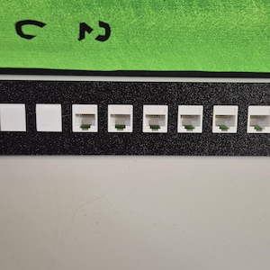 Puede incluir: Una placa de pared de metal negro con ocho puertos RJ-45 blancos para conectar cables de red.