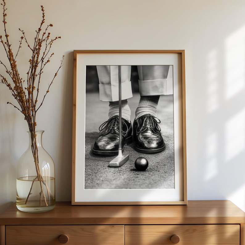May include: Black and white framed print of a golfer putting. The image shows the golfer's feet in black leather shoes, white socks, and light-colored pants. A golf club and ball are in focus.