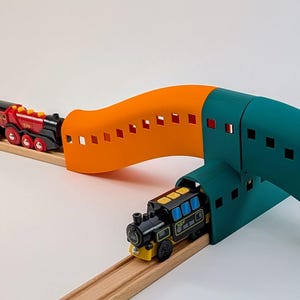 Puede incluir: Un tren de juguete con un puente verde y naranja, un tren negro y amarillo y vías de madera.