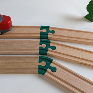 Könnte beinhalten: Ein hölzernes Spielzeug-Eisenbahnset mit grünen Verbindungsstücken. Die Schienen sind aus Naturholz und haben eine leichte Kurve. Ein roter Spielzeugzug befindet sich auf den Schienen.