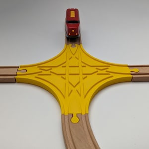 Può includere: Un binario di legno giallo con un treno rosso sopra. Il binario ha la forma di una croce con una sezione curva in basso.