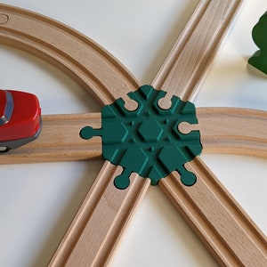 Könnte beinhalten: Eine rote Spielzeug-Lokomotive mit gelben Details befindet sich auf einem hölzernen Gleis. Das Gleis ist mit einem grünen Kunststoff-Weichenstück verbunden. Ein grüner Holzbaum befindet sich im Hintergrund.