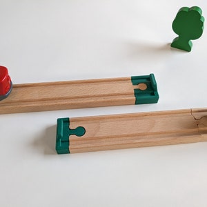 Puede incluir: Dos vías de tren de madera con piezas finales verdes. Un tren rojo está en la vía de la izquierda y un tren negro está en la vía de la derecha.
