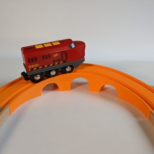 May include: A red toy train engine with the word "BRIO" and "JR 102" printed on the side, going over an orange wooden bridge.