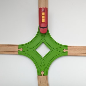 Può includere: Un set di binari per treni in legno verde con un vagone rosso su uno sfondo bianco.