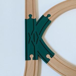 May include: A wooden train track set with a green plastic points track. The points track has a decorative design.