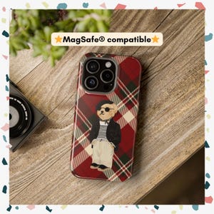 May include: A red and black plaid phone case with a cartoon bear wearing a beret and sunglasses. The case is compatible with MagSafe.