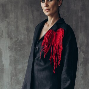 Puede incluir: Una mujer lleva una chaqueta negra de lino con un adorno en forma de coraz&oacute;n rojo en el lado izquierdo. El coraz&oacute;n est&aacute; hecho de tela roja deshilachada.