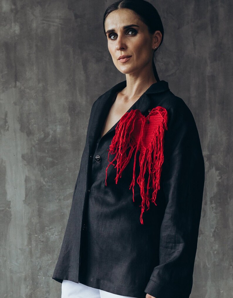 Puede incluir: Una mujer lleva una chaqueta negra de lino con un adorno en forma de coraz&oacute;n rojo en el lado izquierdo. El coraz&oacute;n est&aacute; hecho de tela roja deshilachada.