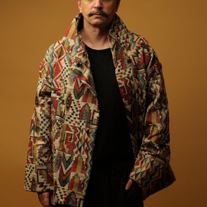 May include: A man wearing a multi-coloured patterned jacket with a black shirt and black trousers.