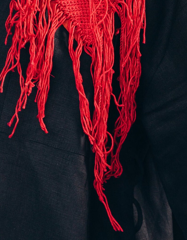 Puede incluir: Una bufanda roja con flecos y hebras largas y delgadas que cuelgan. La bufanda est&aacute; hecha de un material suave y tejido y tiene un aspecto texturizado.