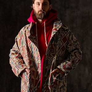 Könnte beinhalten: Eine langärmelige Jacke mit einem farbenfrohen geometrischen Muster. Die Jacke ist aus gewebtem Stoff und hat eine lockere Passform. Das Model trägt darunter ein rotes Kapuzenpullover.