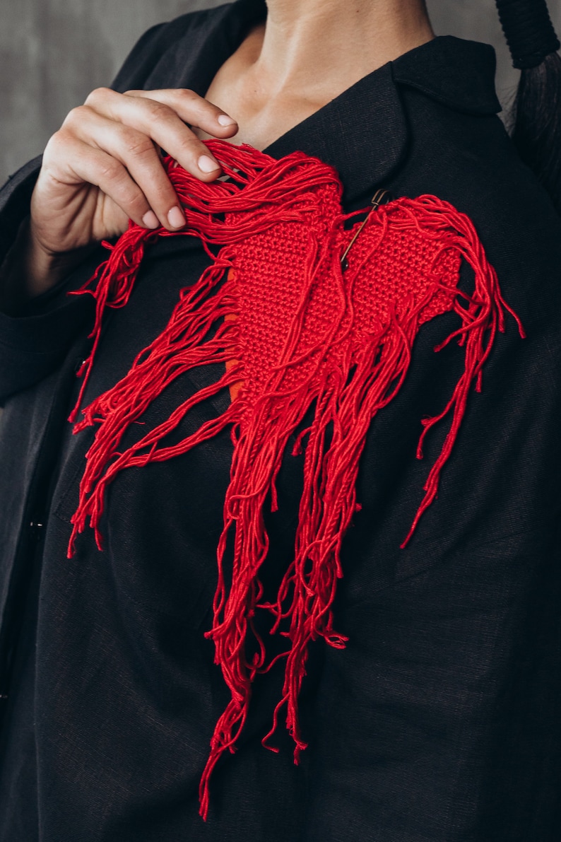 Puede incluir: Un coraz&oacute;n rojo de ganchillo con flecos largos que cuelgan de una chaqueta negra.