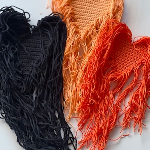 Puede incluir: Tres parches de coraz&oacute;n de ganchillo con flecos. Los parches son negros, naranja y melocot&oacute;n.