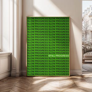 Może przedstawiać: Oprawiony wydruk artystyczny z zielonym tłem i powtarzającymi się słowami "SLOW PROGRESS", z "STILL PROGRESS" w jaśniejszym odcieniu zieleni. Grafika jest wystawiona w pokoju z oknem i sofą.