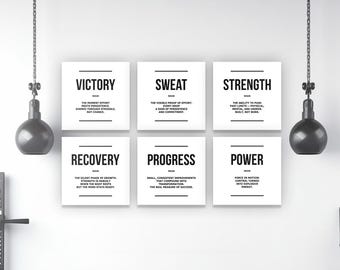 May include: A gym interior featuring six white square motivational posters with black text. Below, a row of black kettlebells sits on a shelf. Two hanging weights and a weight rack are also visible, creating a fitness-themed setting.