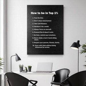 May include: A black framed canvas print with white text that reads "How to be in Top 1%" followed by a list of ten rules for success. The print is hanging on a white wall, with a desk and chair in front of it.
