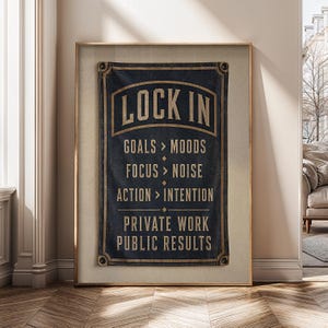 Può includere: Uno stendardo rettangolare in tessuto blu scuro con testo dorato che riporta LOCK IN, GOALS > MOODS, FOCUS > NOISE, ACTION > INTENTION, PRIVATE WORK e PUBLIC RESULTS. Lo stendardo presenta occhielli metallici agli angoli ed è incorniciato.