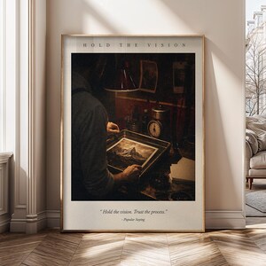 May include: A framed wall art print featuring a dark, moody scene of a person developing a photograph in a tray. The text HOLD THE VISION appears at the top, and the quote Hold the vision. Trust the process. - Popular Saying is at the bottom.