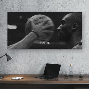 May include: Black and white photograph of a basketball player in action. The image shows a close-up of a basketball being handled, with the text "lock in." printed on the image. The image is displayed on a wall.
