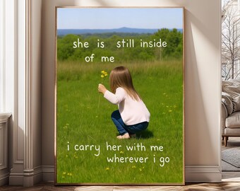 May include: A framed print featuring a child in a field of green grass, holding yellow flowers. The text "she is still inside of me" and "i carry her with me wherever i go" is written on the print.