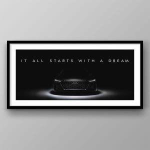 以下が含まれることがあります： 黒いフレームに入ったプリント。黒いアウディ車と「IT ALL STARTS WITH A DREAM」の白い文字。車は暗い背景の中でスポットライトで照らされています。この画像は、ドラマチックでコントラストの高い構図です。