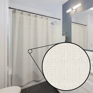 May include: A white shower curtain with a geometric pattern of thin black lines forming a grid. The curtain is hung on a black shower rod.