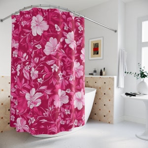 May include: A pink floral shower curtain with white flowers and green leaves. The curtain is hanging in a bathroom with a white bathtub and a white tiled wall.