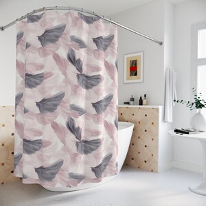 May include: A white shower curtain with a pink and gray feather pattern. The curtain is hanging in a bathroom with a white bathtub and a tiled wall.