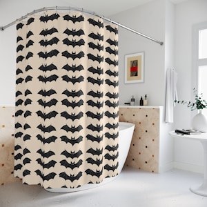Op de afbeelding: Een beige douchegordijn met een zwart vleermuispatroon. Het gordijn hangt in een badkamer met een wit bad en een witte betegelde muur.