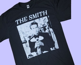 May include: Black t-shirt with a white graphic of Morrissey, the lead singer of The Smiths, wearing a suit and holding a flower. The text "THE SMITHS" is printed above the image.