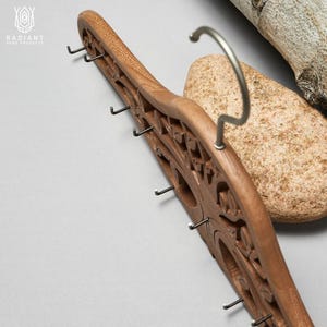 May include: A wooden coat rack with a carved tree design and multiple metal hooks. The rack is brown and has a natural wood finish.