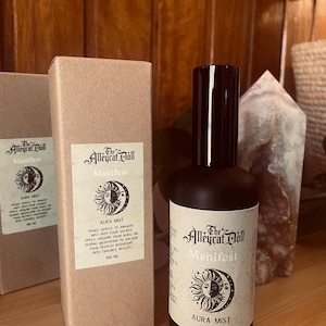 May include: A 100 ml matte black spray bottle and matching tan cardboard box labelled The Alleycat Doll Manifest Aura Mist. The label features a sun and moon graphic with text instructing to shake gently to awaken the mist into your sacred space.