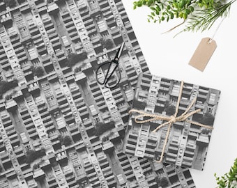 May include: Black and white wrapping paper with a repeating pattern of apartment buildings. The paper is wrapped around a gift box tied with twine.