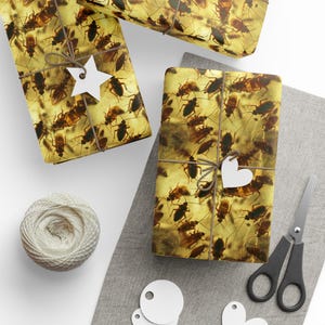 Peut inclure: Trois boîtes cadeaux emballées dans du papier brun avec un motif de cafards. Les boîtes sont décorées d'étoiles et de cœurs en papier blanc.