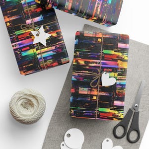 May include: Two rectangular gifts wrapped in black paper with a vibrant, horizontal digital glitch pattern in rainbow colours. Each package is tied with brown twine and features a white paper gift tag, one star-shaped and one heart-shaped.