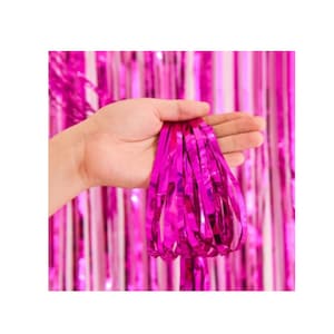 May include: Bright pink metallic fringe held in a hand, with a matching background of vertical fringe. The shiny material reflects light, creating a festive and celebratory atmosphere. Ideal for party decorations or photo backdrops.