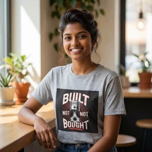 Puede incluir: Una camiseta gris con las palabras "BUILT NOT BOUGHT" en blanco, junto con un gráfico de pistón de motor. La camiseta la lleva una persona sonriendo a la cámara.