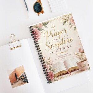 May include: A spiral-bound journal with a cream cover featuring pink roses, a gold cross, and the text Prayer and Scripture Journal. Below the text is an illustration of an open Bible and a pink teacup with a gold cross, plus a Bible verse.