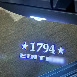 May include: A close-up of a car's interior, featuring the illuminated text "1794 EDITION" in white with blue accents. The text is flanked by stars, and the background is a textured, dark surface.