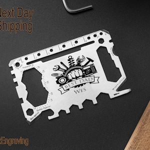 May include: A silver multi-tool credit card sized tool with a ruler, bottle opener, box opener, and other tools. The tool has a black and white design that says "Best Dad Wes".