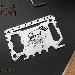May include: A silver multi-tool with a ruler, bottle opener, and other tools. The tool has a black and white design with the word "DAD" and the names "KAYLE", "CHASE", and "ELIZA" printed on it.